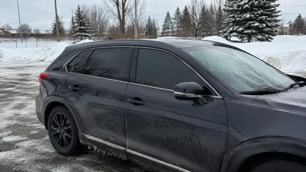modern car with tinted windows parked in a Canadian winter setting, with snow, road salt, and cold weather outside